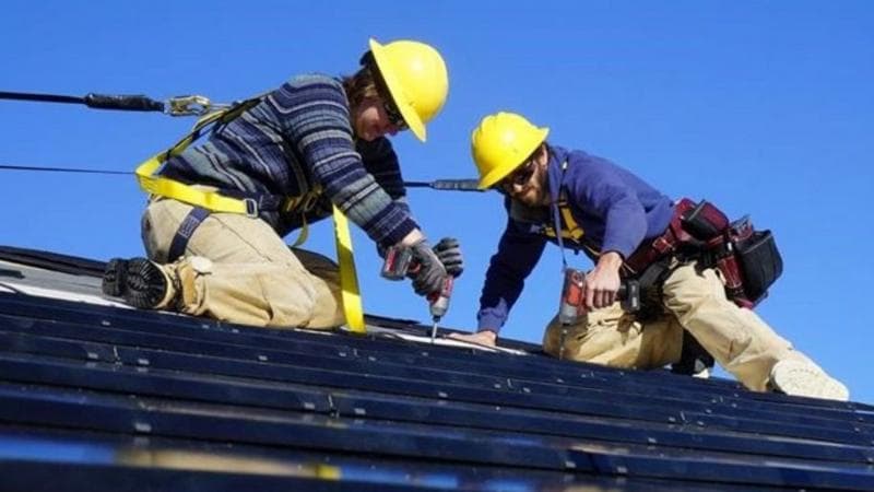 Kate Collardson on a solar roof, wearing a harness and yellow hard hat.