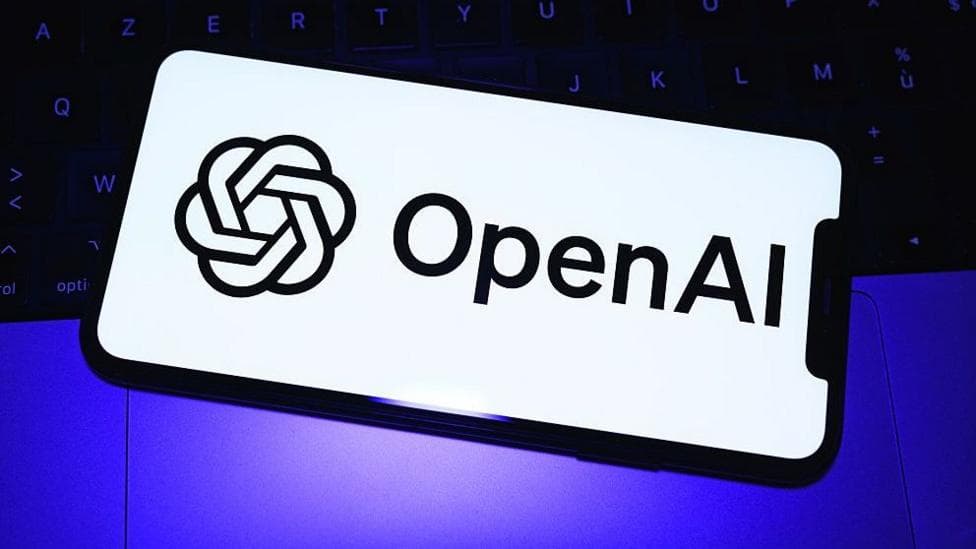 The OpenAI logo in black font on a white phone background over a purple light and black keyboard