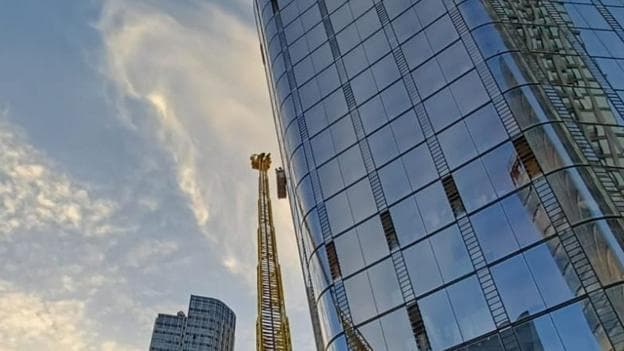 A large yellow ladder is seen extending up the side of a glass walled tower block.