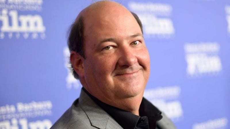 A smiling, bald man is wearing a grey jacket and black shirt
