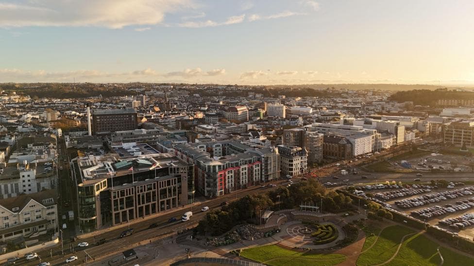 Drone shot of St Helier, Jersey. It shows buildings along a road. Behind there are many more buildings stretching off into the distance.