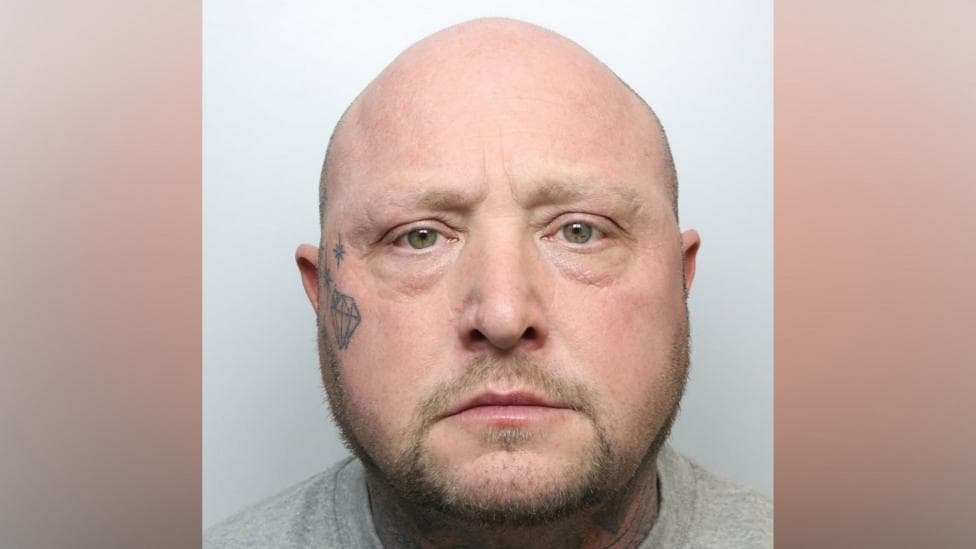 A police mugshot of David Barraclough. He has a bald head and tattoo of a crystal and a number of stars on his right cheek.
