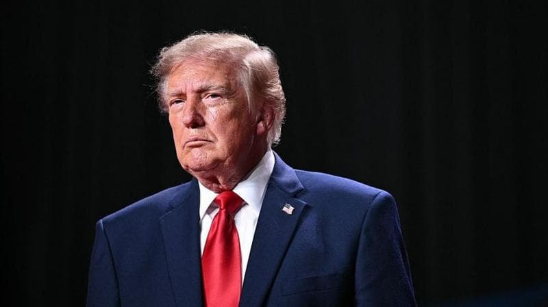 Donald Trump stands in front of a black curtain.