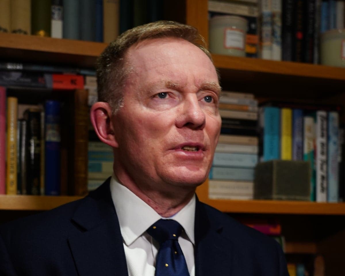 Sir Chris Bryant, in a dark suit and tie, speaks in front of bookshelves