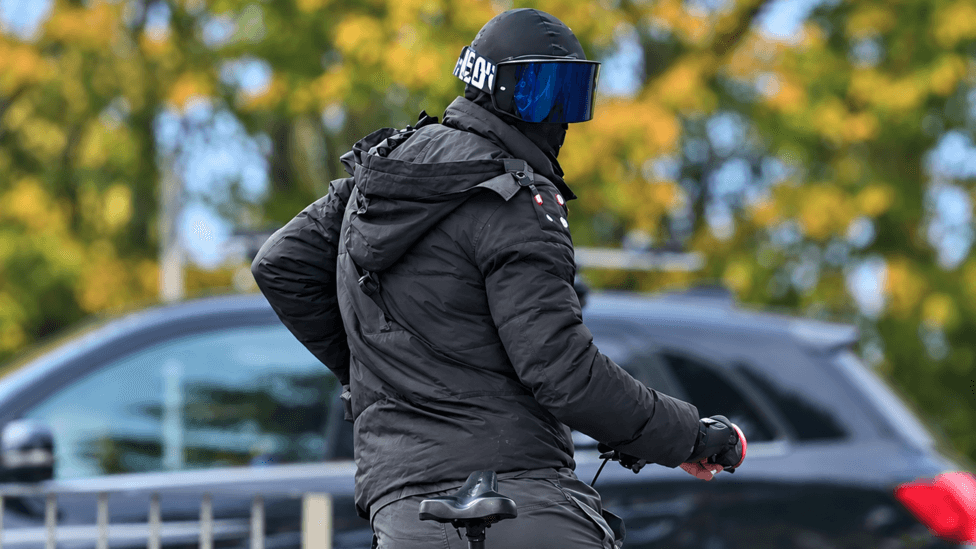 A man on a bike wearing a balaclava and large protective glasses so his face is unrecognisable.