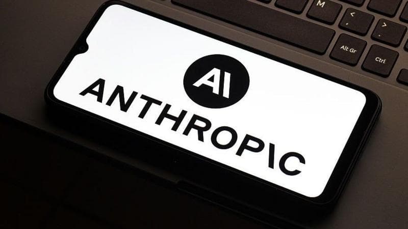 Anthropic logo on a smarthphone which is lying flat on the mousepad of a laptop. Only a partial keyboard of the laptop is visible.