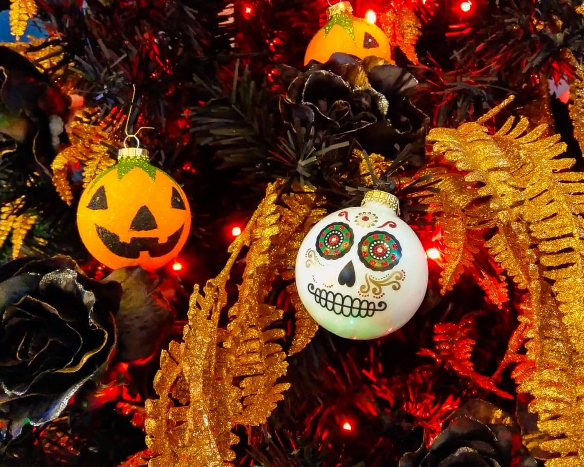 Closeup of a Halloween tree with jack-o'-lantern and sugar skull baubles amid gold tinsel and black roses