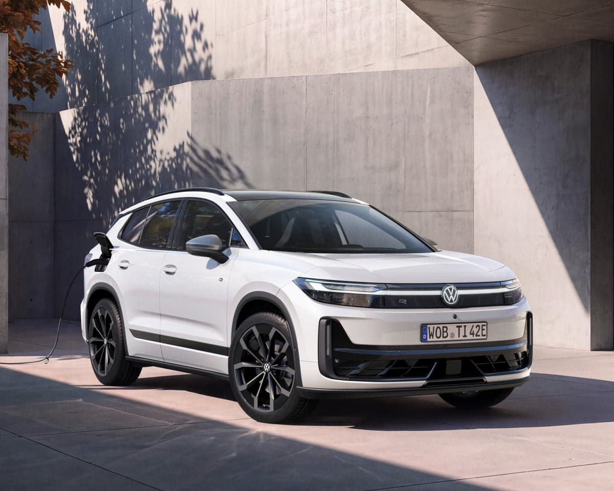 A white electric SUV, the ID. Tiguan, is parked and charging near a concrete building