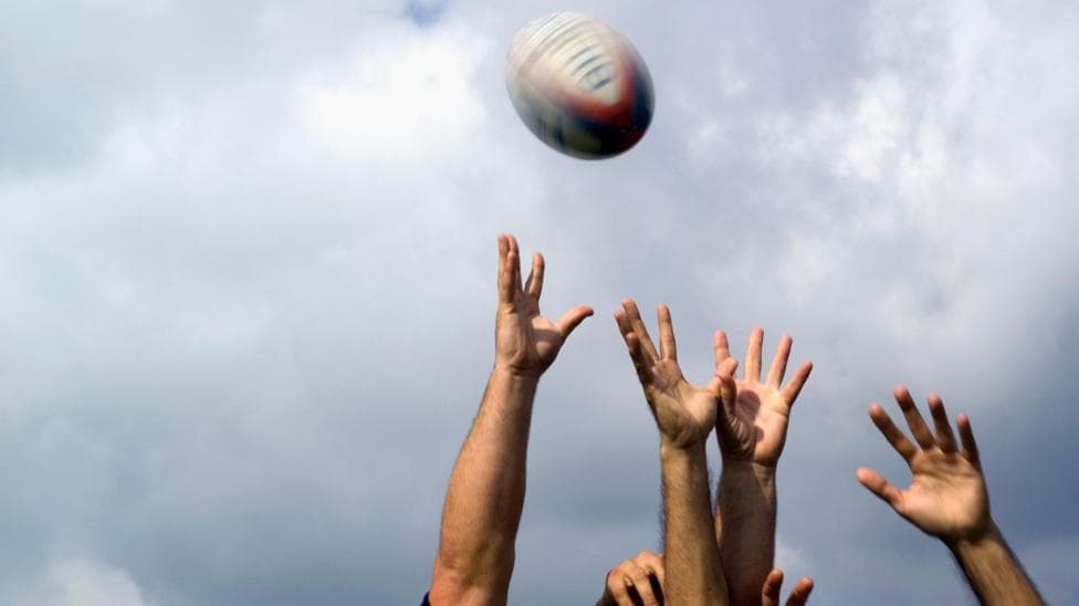 Hands reach for a rugby ball flying through the air
