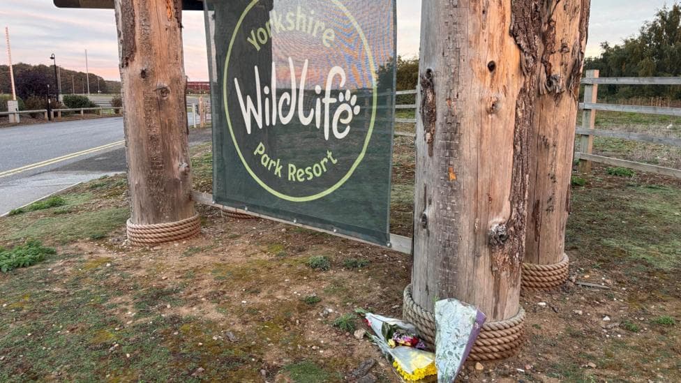 Flowers below a green sign hung between two wooden posts. On the sign it says: Yorkshire Wildlife Park Resort.