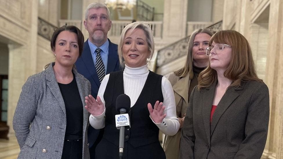 Five people stand around a microphone in Stormont's Great Hall