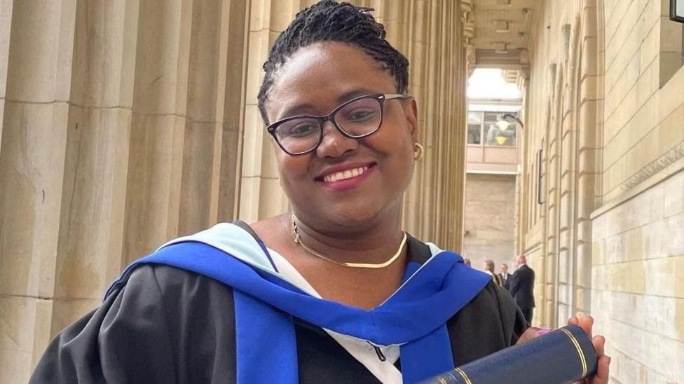 Dr Gomo, who is wearing black graduation robes, smiles as she holds a University of Dundee scroll. She is also wearing glasses.