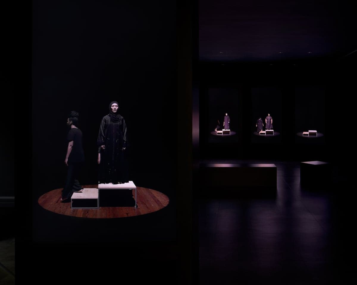 Gabrielle Goliath's Elegy installation shows video screens of robed figures on illuminated platforms in a dark gallery
