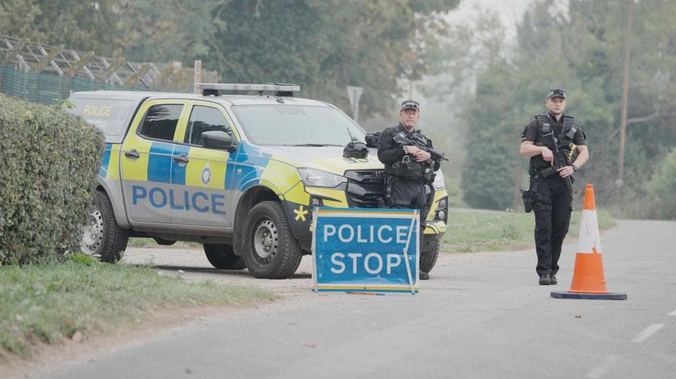 Police stand near a stop sign and a police vehicle near RAF Fairford