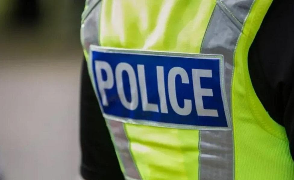 A close-up of the back of a police officer. The officer is wearing a green hi-vis jacket with the word "police" printed on it.