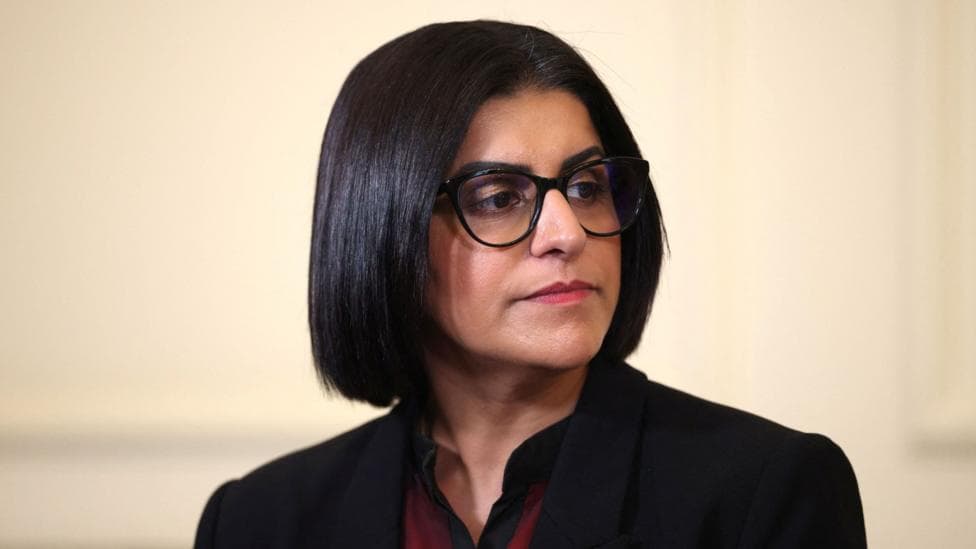 Headshot of Shabana Mahmood looking off-camera wearing black glasses, a black jacket and red shirt.