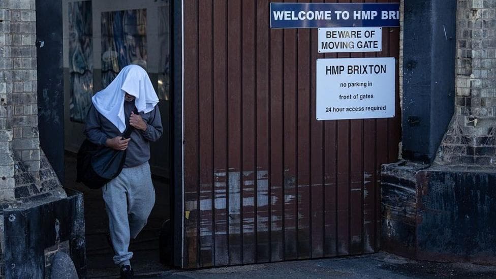 An inmate walks free from HMP Brixton with a while towel over his head