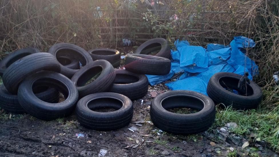 A number of black tyres discarded on a roadside.