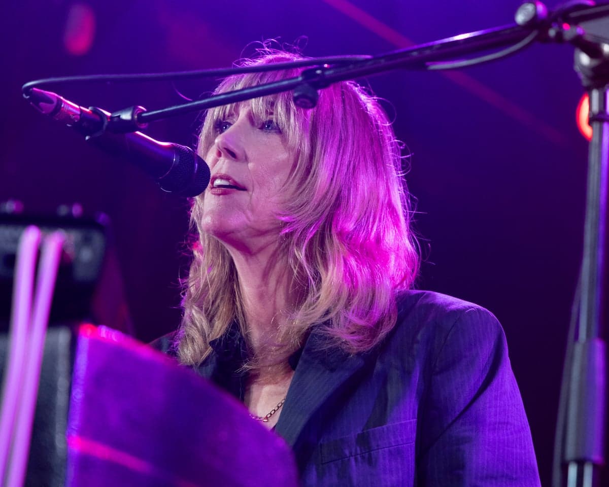 Beth Orton sings into a microphone under purple stage lighting during a performance