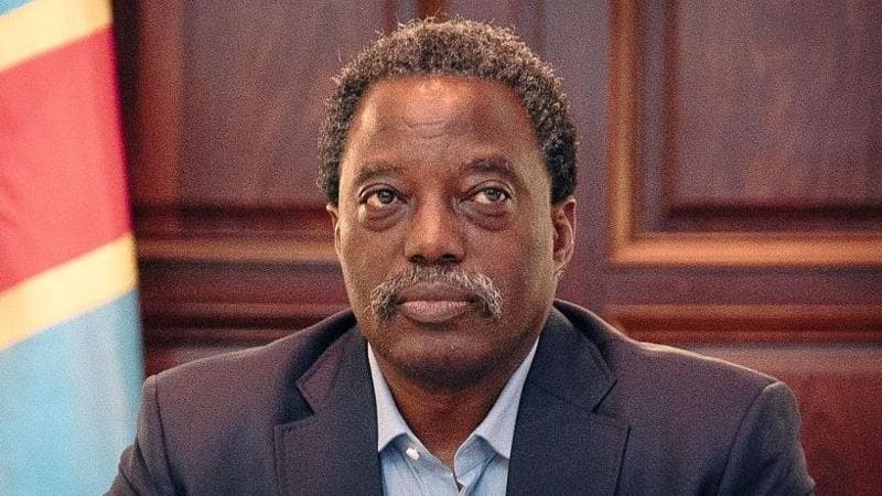 Former Democratic Republic of Congo president Joseph Kabila in a dark suit and blue shirt and a Congolese flag in the background