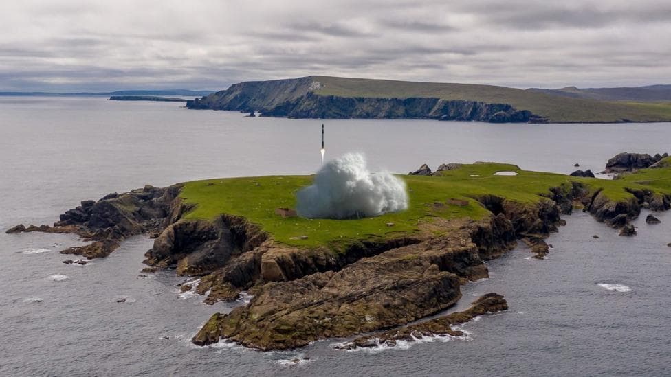 A mock up showing a rocket launch at SaxaVord. The rocket is rising vertically from the launch site on a rocky peninsula at Unst. The rocket leaves a cloud of smoke behind it.