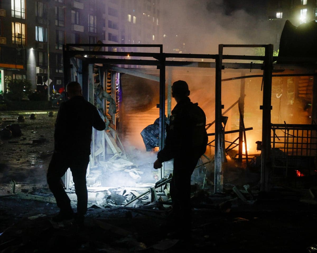 Rescuers stand amid rubble and smoke at a burning building after a drone strike in Kyiv