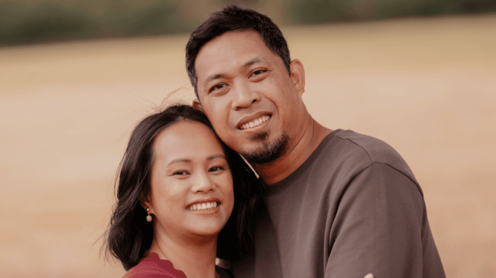 A man and woman, both with dark hair, hugging and smiling.