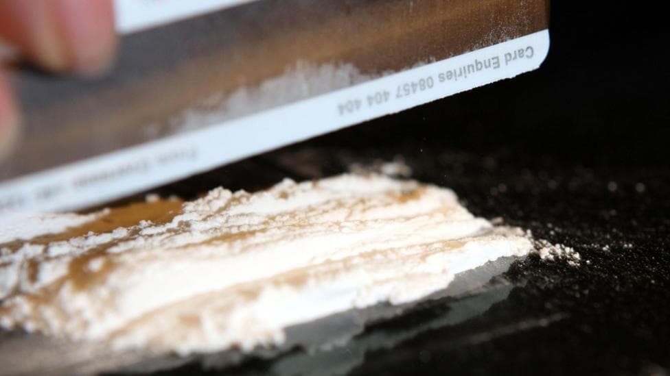 Mock-up picture of a person cutting cocaine, using what looks like a credit card.