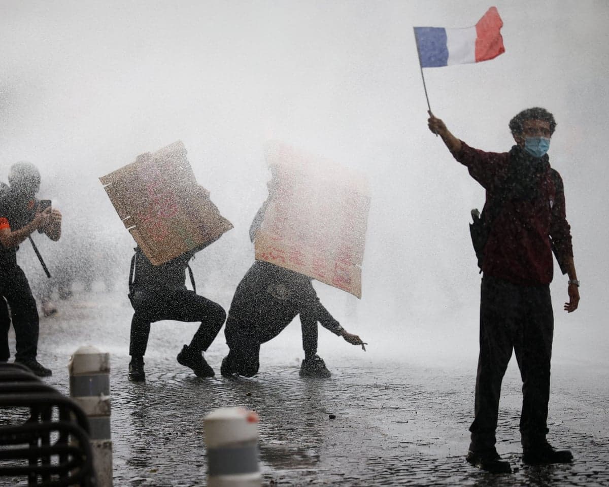 A masked protester waves a French flag as police use water cannon amid clashes