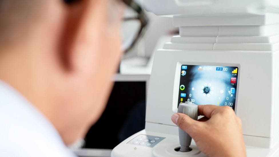 Rear view of an ophthalmologist using a modern eye test equipment tool to perform a vision exam with his patient at an ophthalmologist's clinic