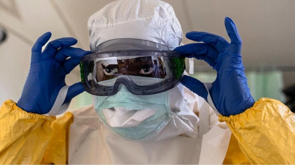 A medical worker in Kenya dons Ebola protective gear: a yellow suit, blue gloves, white hood, an eye mask and face mask.