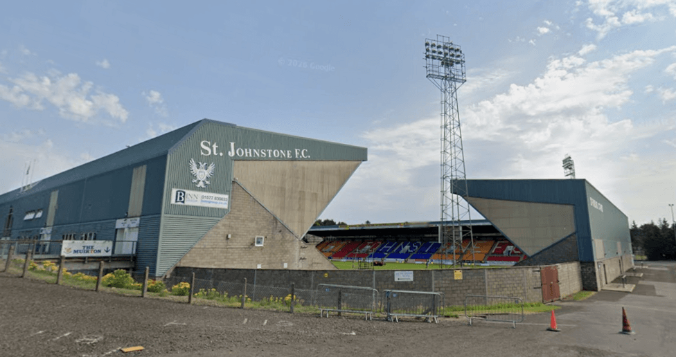 A football stadium from the outside. The pitch is visible between two of the stands