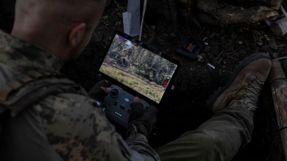 A solider rests a Starlink-connected phone on his body armour to communicate with other troops