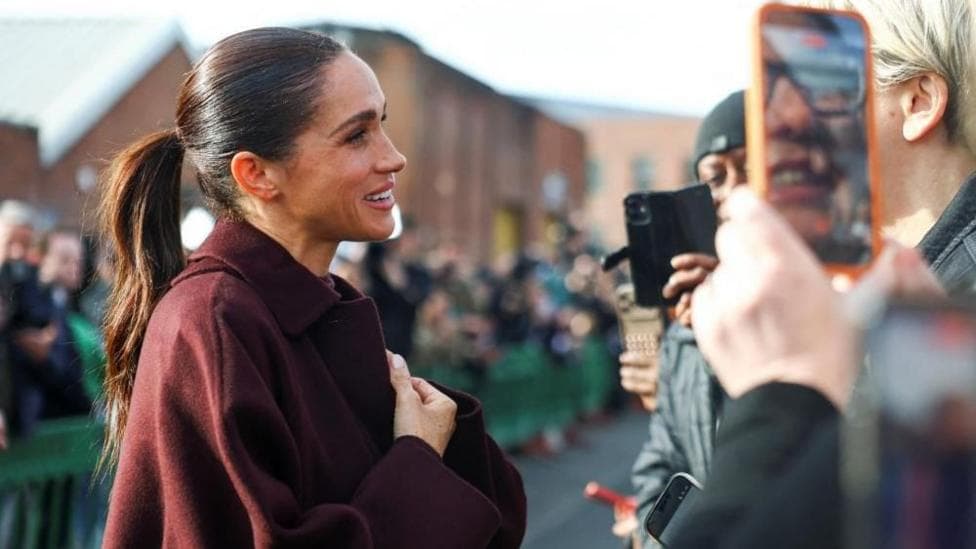 The Duchess of Sussex clutches her hands and smiles warmly as she greets fans waiting for her and Harry in Nottingham