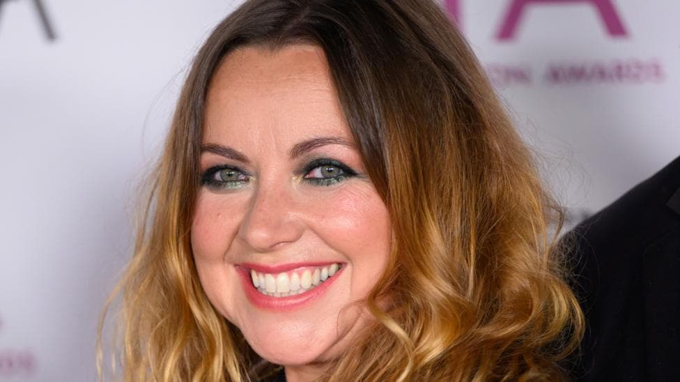 A close up shot of Charlotte Church. Her wavy hair is different shades of brown, and she wears sparkly green eyeliner and smiles and the camera.