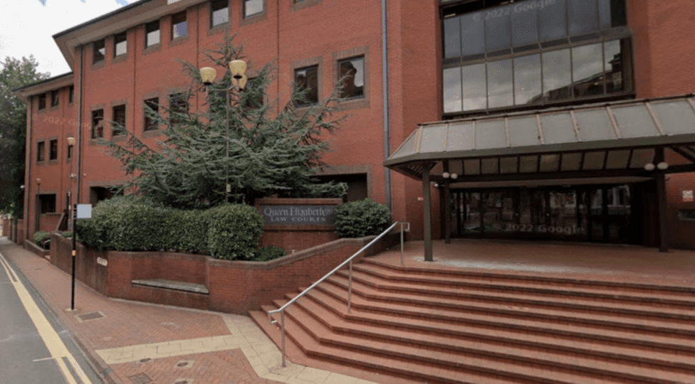 The entrance to a large red brick building with red brick steps leading to black-framed doors.