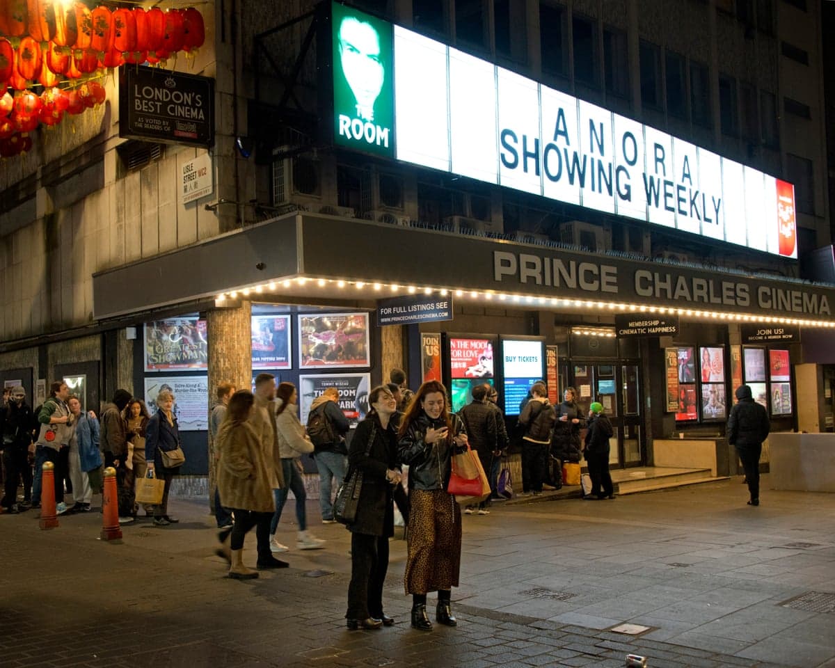 People queue outside the illuminated Prince Charles Cinema at night in London