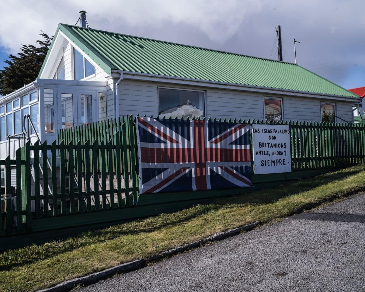 A union flag on a fence outside a property with white panelled walls and a green roof.