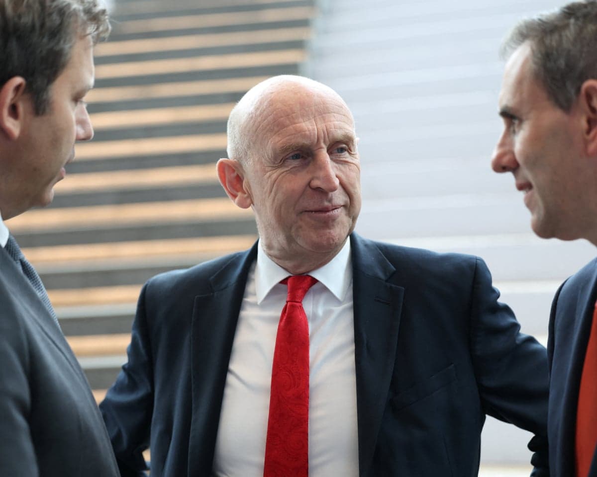 Lars Klingbeil, John Healey, and Jim Chalmers converse closely indoors near stairs