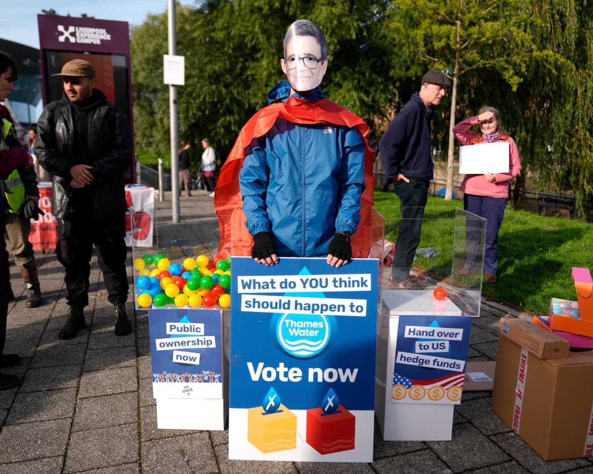 A protester wears an Andy Burnham mask and cape, holding a sign about Thames Water's future