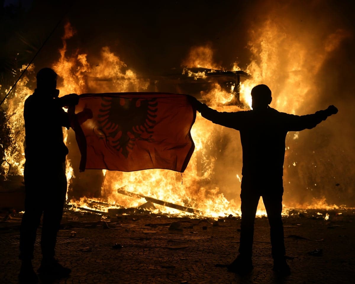 Protesters hold an Albanian flag in front of a burning building during clashes in Tirana.