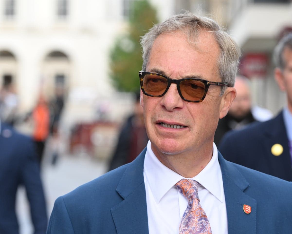 Nigel Farage, wearing sunglasses and a blue suit, speaks during a walkabout outdoors