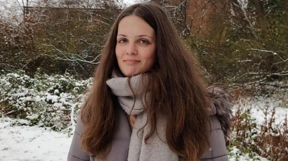Liberty in a grey puffer jacket and grey scarf with long brown hair stood outside in the snow