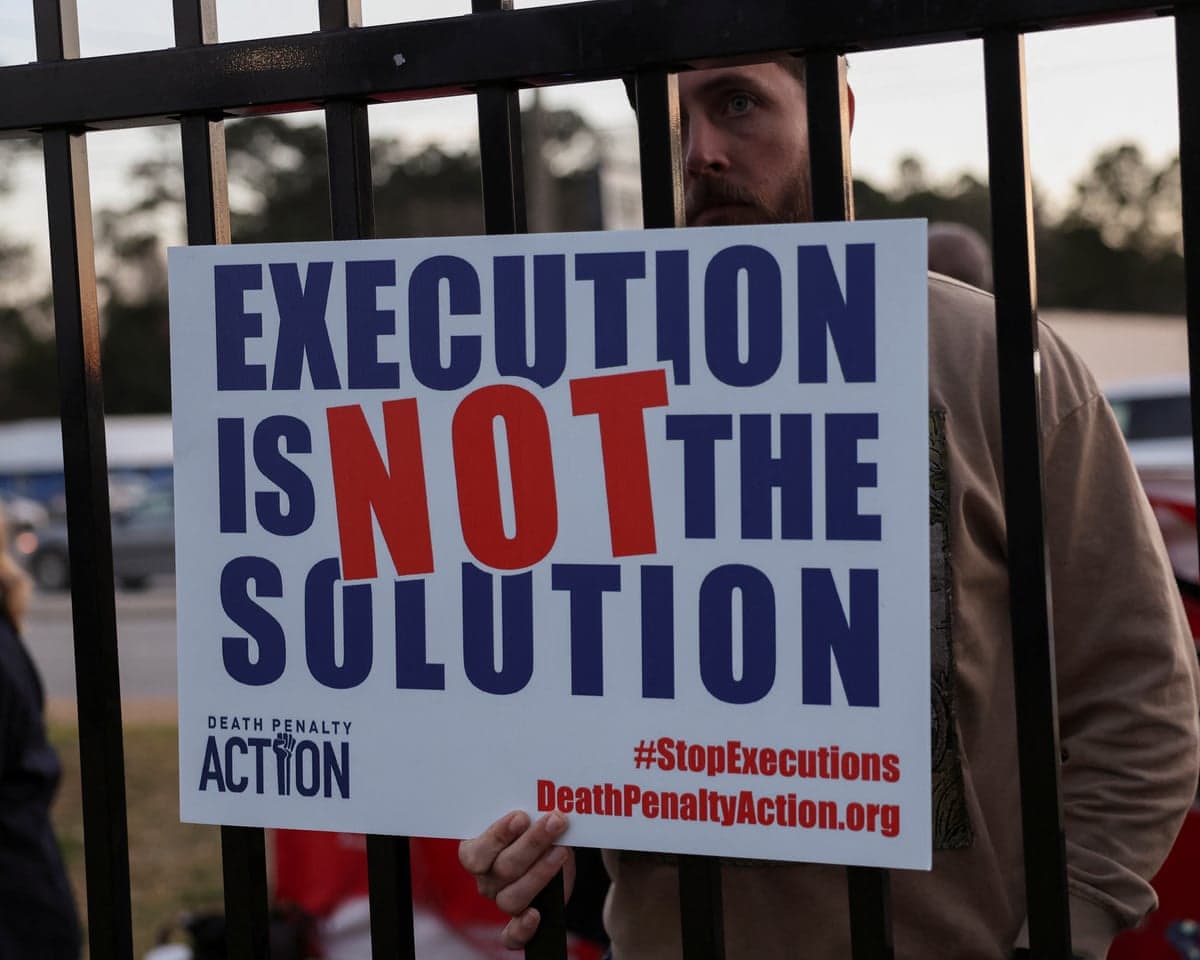A demonstrator behind prison bars holds a sign reading "Execution Is Not The Solution"