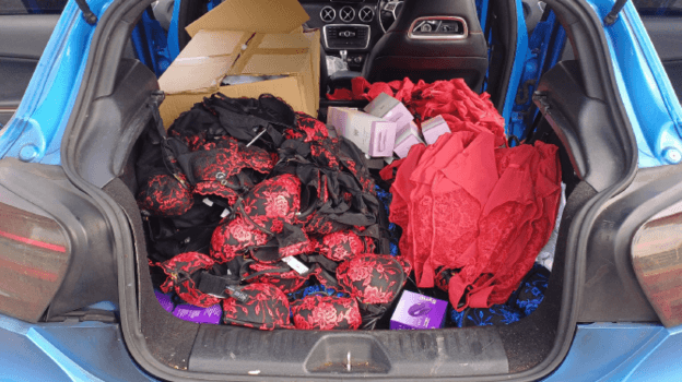 A pile of lingerie and boxed sex toys in the boot of a blue car