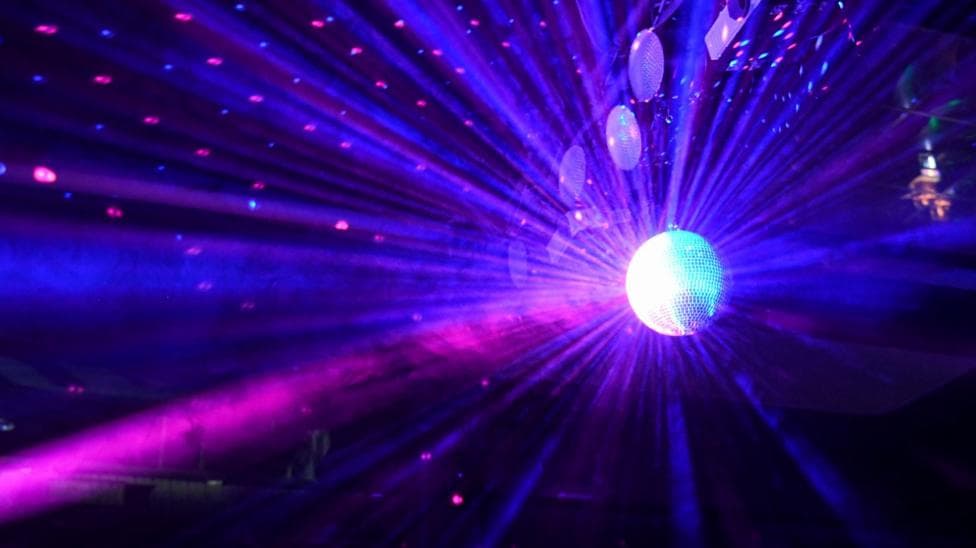 A disco ball shines a purple light across a dark dance floor.