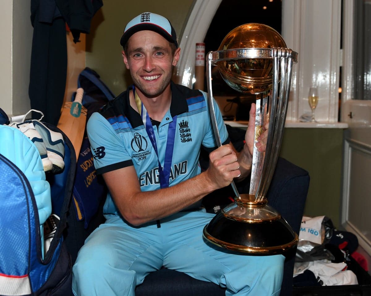 Chris Woakes holding the World Cup trophy with the winners' medal around his neck in the dressing room