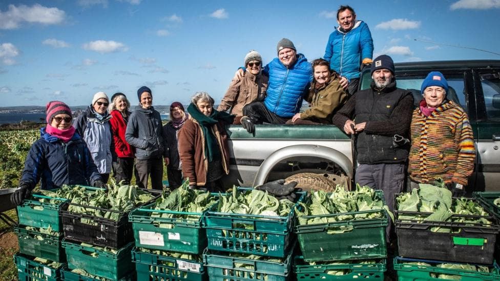 Twelve people standing in a field with crates of vegetables in front of them.