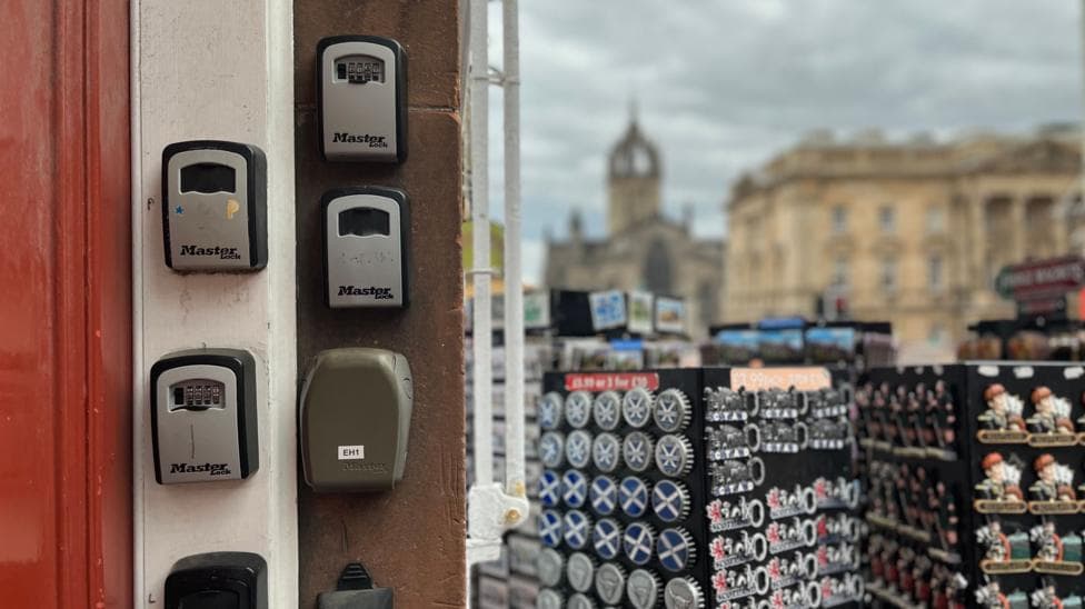 Black and grey key boxes are attached to the wall next to the entrance to a block of flats, which are next to a tourist gift shop.