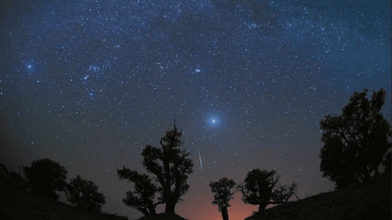 A meteor strikes across a dark blue star-filled night sky